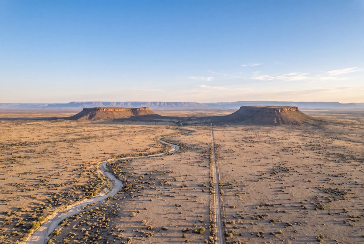 Flat-topped mountains and a lone road across a remote plain at golden hour