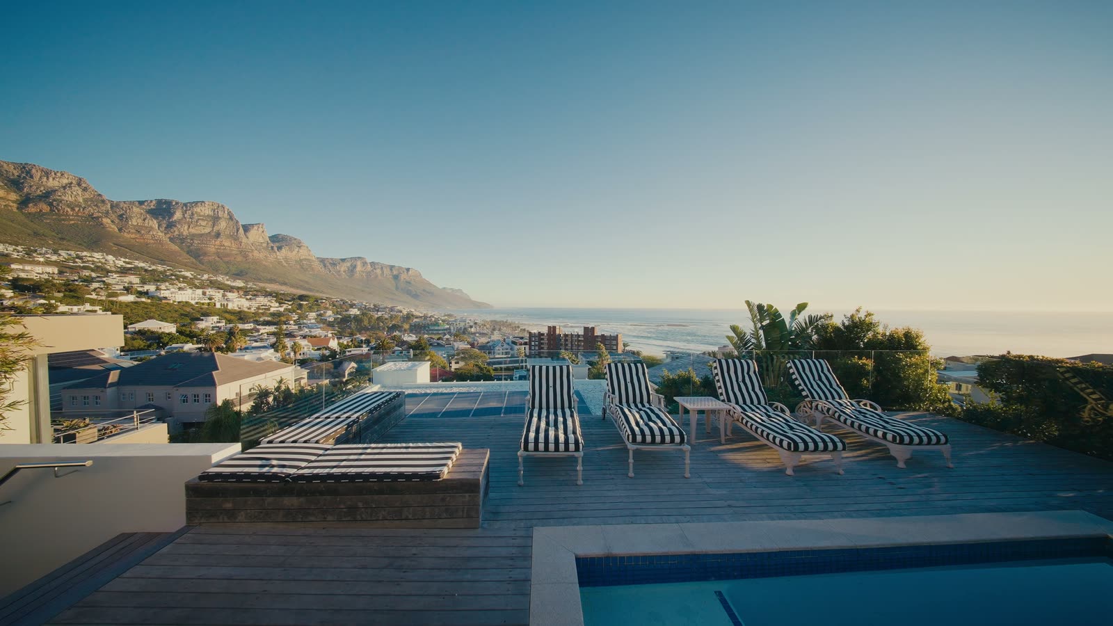 The rooftop terrace of Villa Twelve Apostles at golden hour, loungers beside the pool above Camps Bay Beach