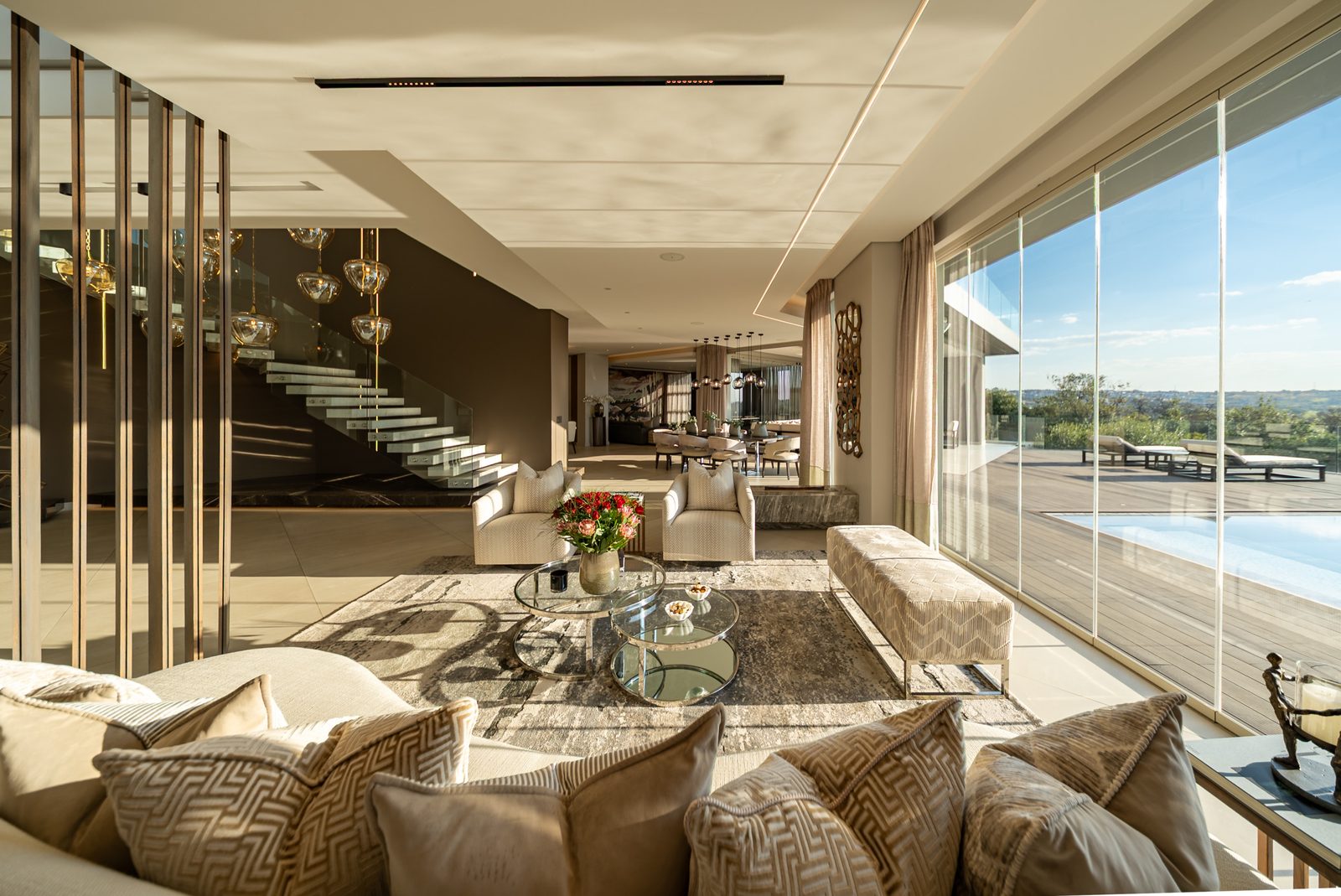 Open plan lounge beneath the curved marble staircase, glass walls to the pool terrace